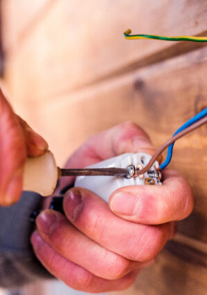 Hands of unrecognizable electrician working with screwdriver, wooden wall